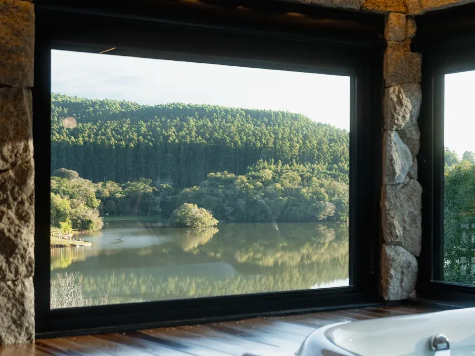Banheira de hidromassagem coberta diante do janelão com vista para o lago