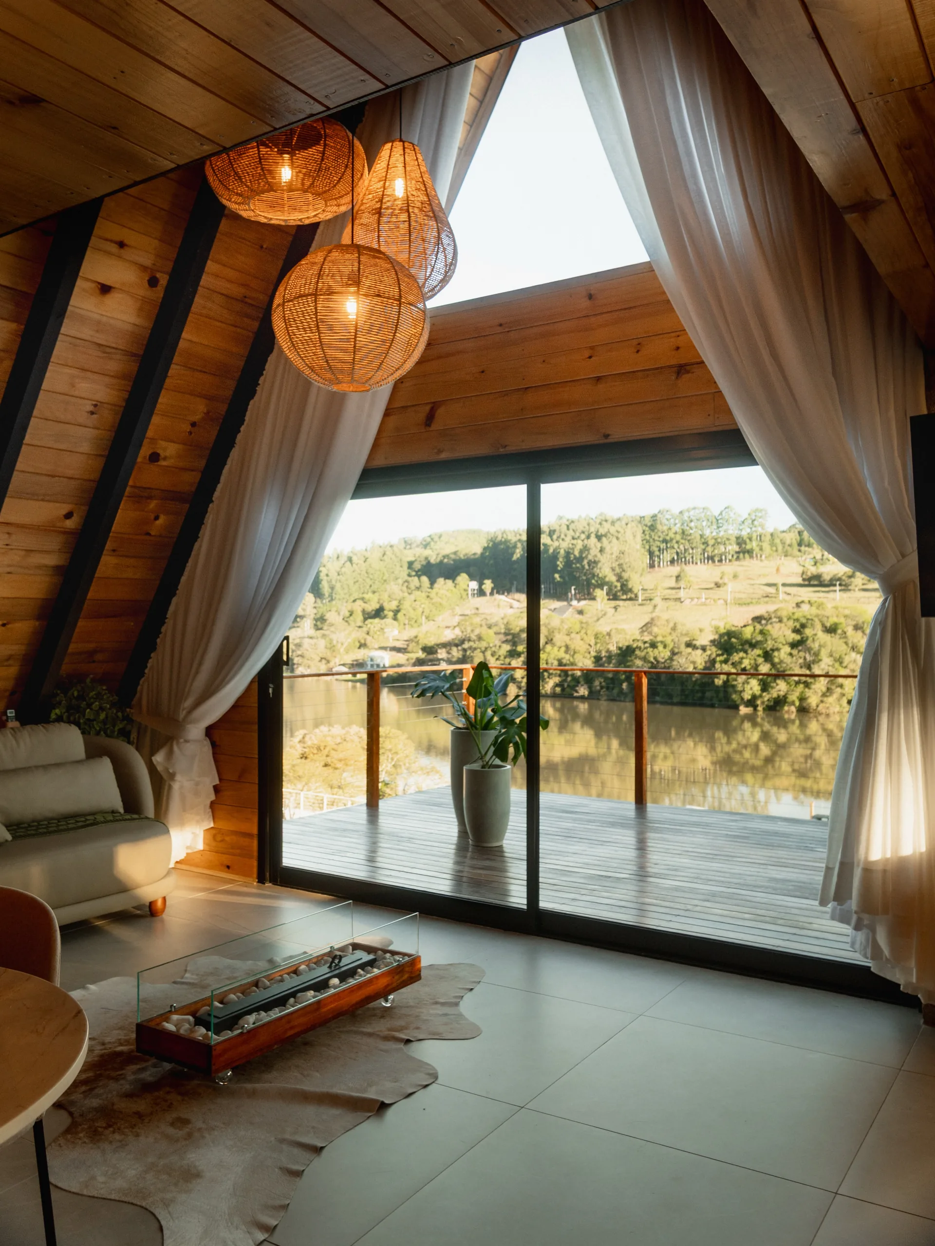Sala da cabana A-frame com a porta de vidro aberta para a sacada e o lago