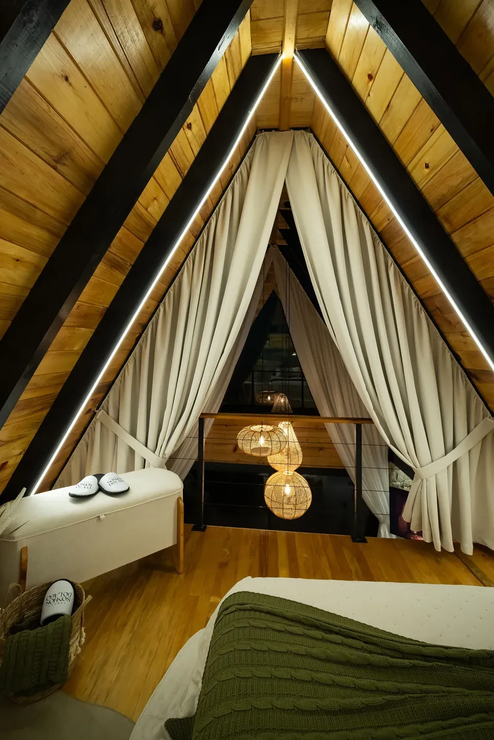 Quarto sob o vértice A-frame, com a cama e as cortinas de linho abertas